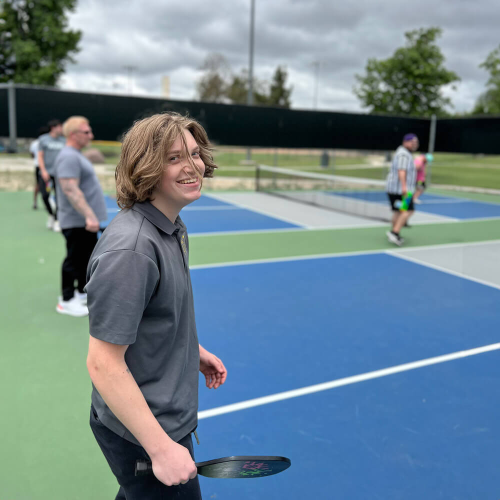 A young man exudes joy as he confidently grasps a tennis racket, radiating enthusiasm for the sport.