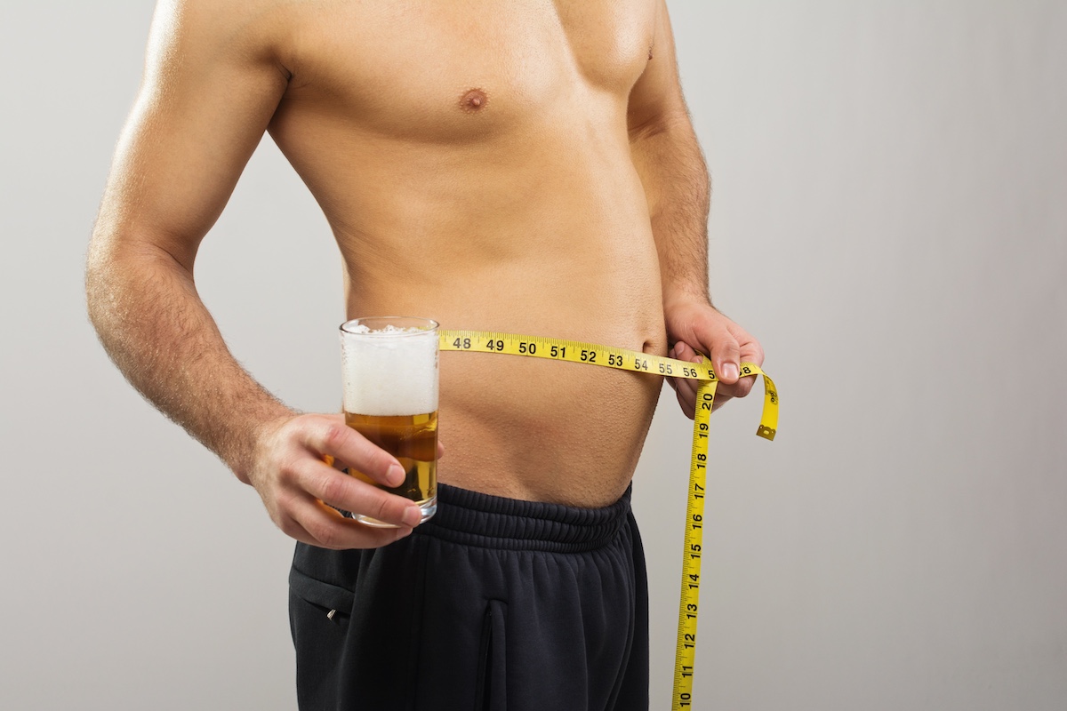 Photo of a man with alcohol belly, holding a beer in one hand a measuring tape in another